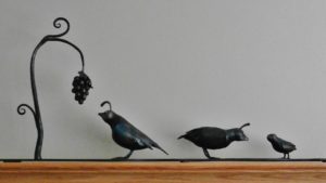 A quail family consisting of a Father, mother and chick in a vineyard with a vine and grapes. All forged and fabricated from mild steel
