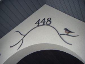 A swooping steel branch with the numbers 448 at the top. To the right a metal robin sits.