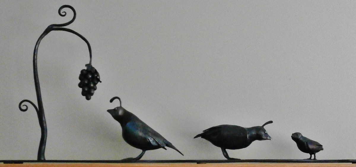 Forged and fabricated family of quail. The father is looking at a cluster of grapes while the doting mother looks after the chick.
