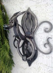 Forged door knocker with a dragon head and horns. The back plate is hand chiseled and also has forged round bar curls.