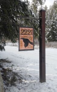 A custom address sign and bracket with numbers and a hand chiseled raven on a hammered copper sheet.
