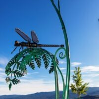 Griffinfly is resting on a large fern leaf, forged and fabricated from new and recycled steel. It is 8 feet tall.